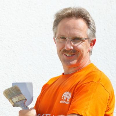 Gerhard Steinlechner lächelt 3/4 zur Kamera gewandt. er trägt ein knallorangenes shirt
